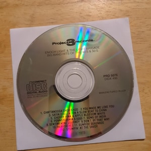 May include: A compact disc by Project 3 Records featuring Enoch Light & The Light Brigade. The CD is silver with black text and includes a tracklist of big band hits from the 40s and 50s. The disc is in a white paper sleeve.