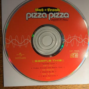 May include: An orange promotional compact disc featuring the Pizza Pizza logo and the text Hot & Fresh Ontario's #1 Pizza. The disc includes a tracklist titled Sample This with songs by Soft Cell, The Buggles, This 'N That, and Cake.