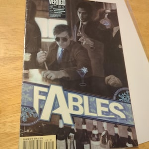 May include: A comic book cover for "Fables" featuring a bar scene with two men in suits. The title "FABLES" is in large, light blue letters. The cover includes the "Vertigo" logo and a barcode.