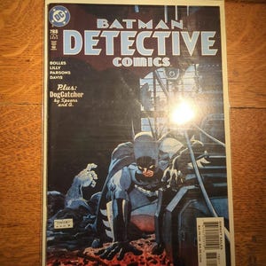 May include: A Batman Detective Comics comic book cover. The cover features Batman in a dark setting with the title "Detective Comics" in large blue letters. The issue number is 788. The cover art is dark and dramatic.