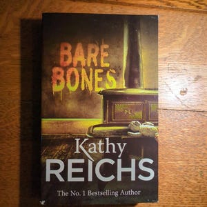 May include: A book titled "Bare Bones" by Kathy Reichs. The cover features a dark, atmospheric illustration with the title in dripping orange letters. The author's name is in large white letters, with the text "The No. 1 Bestselling Author" below.