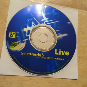 May include: A blue compact disc with the text "Live" in yellow. The disc features the text "Gene Harris & The Philip Morris All-Stars" and the Compact Disc Digital Audio logo. The CD is on a white paper sleeve.