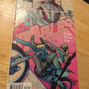 May include: A comic book cover for "Fables" with a pink and blue color scheme. The cover features a person riding a motorcycle, with the title "Fables" in large pink letters. The Vertigo Comics logo is visible.