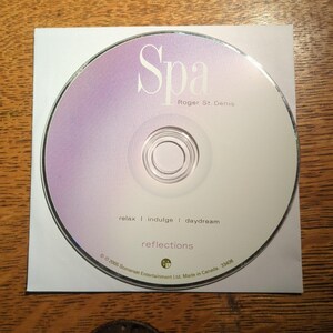 May include: A CD with a white and purple gradient design. The word "Spa" is at the top, with "Roger St. Denis" below it. The text "relax | indulge | daydream" and "reflections" are also visible.