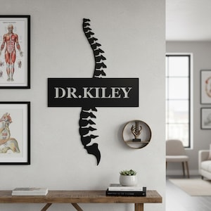 Peut inclure: Décoration murale en métal noir représentant une colonne vertébrale avec le nom "DR. KILEY" en lettres blanches. L'œuvre est fixée sur un mur blanc, avec des schémas anatomiques encadrés et une petite étagère avec une sculpture de colonne vertébrale.