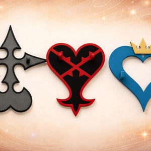 Peut inclure: Trois crochets muraux décoratifs en forme de symboles d'un jeu vidéo. Le premier est un design gris en forme de croix, le second est un cœur rouge et noir, et le troisième est un cœur bleu avec une couronne dorée.