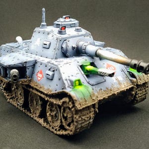 May include: A detailed model tank in shades of gray, with a long gun barrel and visible tracks. The tank has red and green accents, and is covered in mud, giving it a battle-worn appearance. The model has the number "345" on the side.