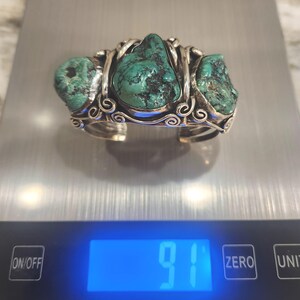 May include: A silver bracelet with three turquoise stones set in a twisted wire design. The bracelet is on a digital scale that reads 91.