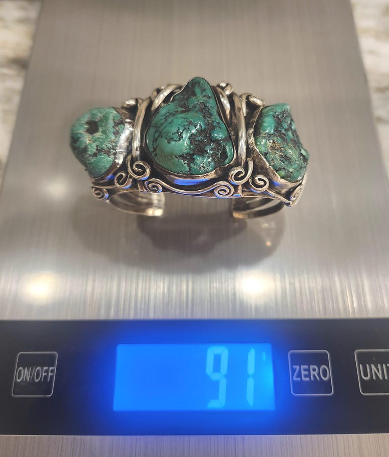 May include: A silver bracelet with three turquoise stones set in a twisted wire design. The bracelet is on a digital scale that reads 91.