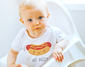 May include: A baby wearing a white onesie with a cartoon hot dog graphic and the text "HOT DIGGITY". The baby has blonde hair and blue eyes and is sitting in a high chair.