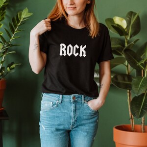 May include: A black t-shirt with the word "ROCK" printed in white in a gothic font.