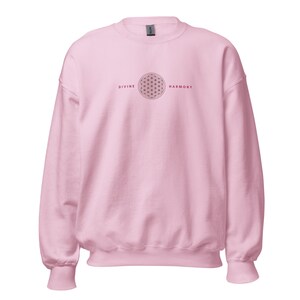 Könnte beinhalten: Hellrosa Sweatshirt mit langen Ärmeln. Auf der Vorderseite steht in Dunkelrot "DIVINE HARMONY" mit einem geometrischen Flower-of-Life-Symbol in der Mitte. Ein lässiges, bequemes Kleidungsstück.