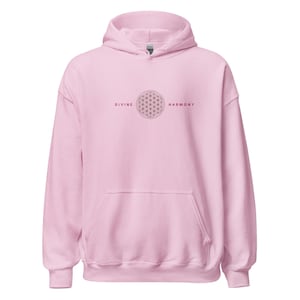Könnte beinhalten: Ein hellrosa Kapuzenpullover mit einer Vordertasche und einer Kapuze. Auf der Vorderseite des Kapuzenpullovers steht der Text "DIVINE HARMONY" über und unter einem geometrischen Lebensblumen-Design.