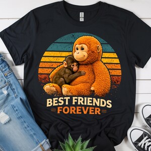 May include: Black t-shirt featuring a graphic of two monkeys hugging, set against a sunset backdrop. The text "BEST FRIENDS FOREVER" is displayed below the image. The shirt is made of a soft material.