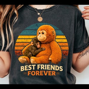 May include: Dark gray t-shirt featuring a graphic of two cartoon orangutans hugging, set against a sunset design with blue, yellow, and orange stripes. The text "BEST FRIENDS FOREVER" is printed below the image.