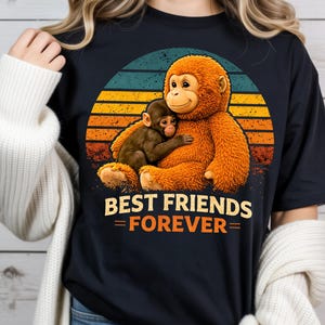 May include: Black t-shirt featuring a graphic of two monkeys hugging, set against a retro sunset design. The text "BEST FRIENDS = FOREVER=" is displayed below the image. The monkeys are brown and orange.