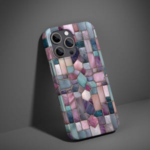 May include: A smartphone case with a mosaic design. The case features a pattern of irregular shapes in shades of pink, purple, blue, and gray. The camera lenses are visible at the top. The case is leaning against a gray surface.
