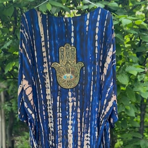 Könnte beinhalten: Ein blaues und weißes Batik-Kimono mit einem goldenen Hamsa-Hand-Anhänger. Die Hamsa-Hand hat blaue Augen.