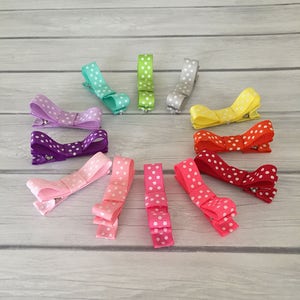 Op de afbeelding: Een set van 12 kleurrijke haarclips met witte stippen. De clips zijn in een cirkel op een houten oppervlak gerangschikt.