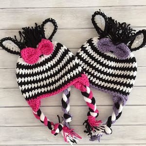 May include: Two crocheted zebra hats with black and white stripes, pink and purple bows, and long braided ties.