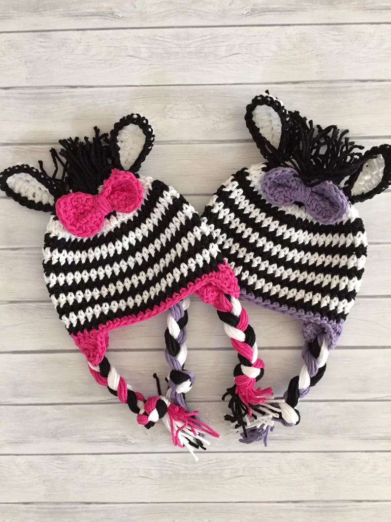 May include: Two crocheted zebra hats with black and white stripes, pink and purple bows, and long braided ties.