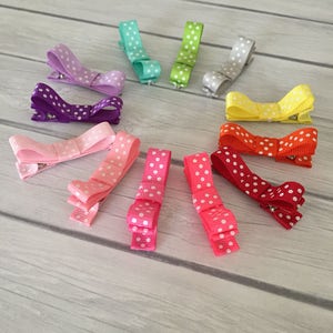 Op de afbeelding: Een set van tien stippen haarclips in verschillende kleuren, waaronder paars, roze, rood, geel, groen en blauw. De clips zijn in een cirkel op een houten oppervlak gerangschikt.