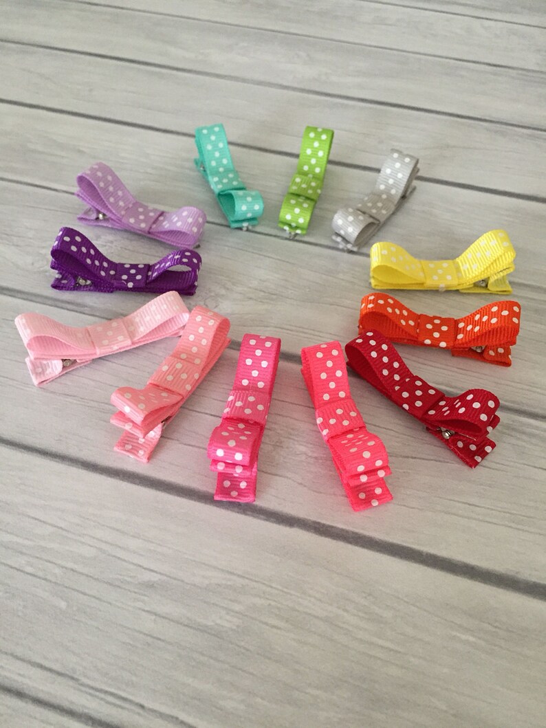 Op de afbeelding: Een set van tien stippen haarclips in verschillende kleuren, waaronder paars, roze, rood, geel, groen en blauw. De clips zijn in een cirkel op een houten oppervlak gerangschikt.