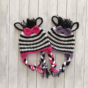 May include: Two crocheted zebra hats with black and white stripes, pink and purple bows, and matching braided ties.
