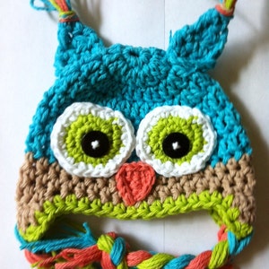 May include: A crocheted owl hat with green, blue, white, and orange yarn. The hat has a long, braided tail with the same colors.