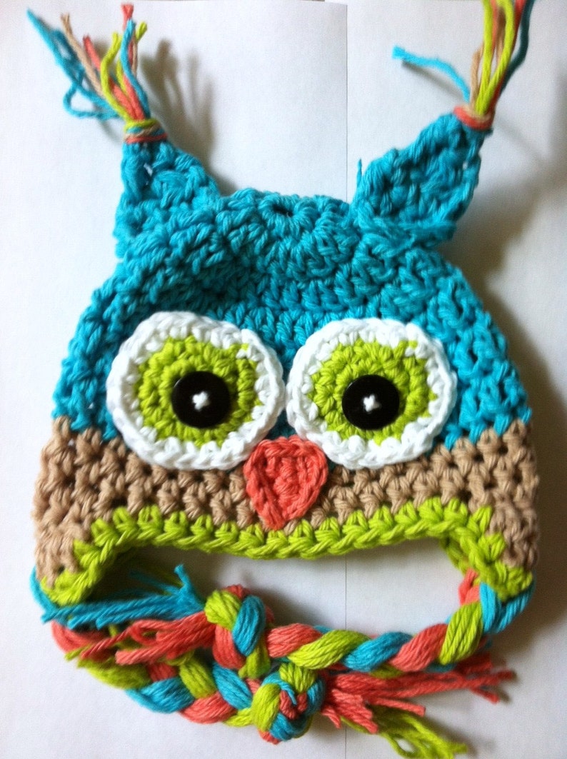 May include: A crocheted owl hat with green, blue, white, and orange yarn. The hat has a long, braided tail with the same colors.