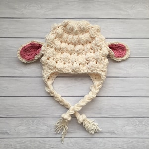 May include: A white crocheted lamb hat with pink ears and a long white braid tied at the bottom.