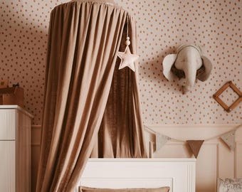 May include: A cozy bedroom scene featuring a bed with a canopy and decorative pillows. The bed has a white headboard and a quilted comforter. A pillow with the text "Oh Girl" is visible. The room is decorated in neutral tones with a star-shaped ornament.