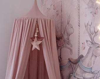 May include: A pink canopy with a star-shaped ornament hangs in front of a wall mural. The mural depicts a carousel scene with a deer, a fairy, and a zebra. A crescent moon-shaped light and butterfly accents add to the whimsical design.