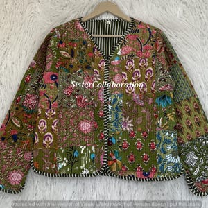 Puede incluir: Una chaqueta acolchada de manga larga con un diseño de patchwork en tonos verde oliva, rosa y azul con motivos florales. La chaqueta tiene cuello en V, un borde a rayas blancas y negras y el texto SisterCollaboration en color blanco.
