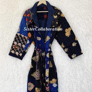 May include: A long, patchwork robe with a navy blue base, featuring various patterned fabric panels in blue, gold, and red. The robe has a belt and the text "Sister Collaboration".