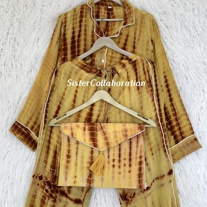 May include: A tie-dye pajama set in shades of yellow and brown, with white trim. The set includes a long-sleeved top, pants, and a matching envelope-style pouch with a tassel. The text "SisterCollaboration" is visible on the clothing.