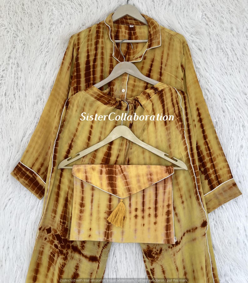 May include: A tie-dye pajama set in shades of yellow and brown, with white trim. The set includes a long-sleeved top, pants, and a matching envelope-style pouch with a tassel. The text "SisterCollaboration" is visible on the clothing.