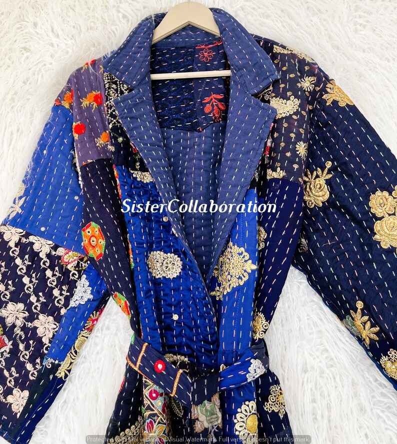 May include: A patchwork robe in shades of blue, with embroidered floral and geometric patterns. The robe features a shawl collar, a matching belt, and is hung on a wooden hanger. The text "SisterCollaboration" is visible on the robe.