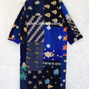 May include: A patchwork robe in shades of blue, black, and gold, with embroidered floral and geometric patterns. The robe has long sleeves and a collar. The text "Sister Collaboration" is visible on the front.