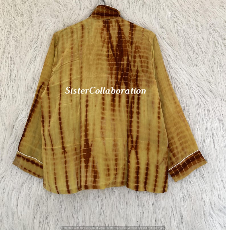May include: A long-sleeved, tie-dye shirt in shades of yellow and brown. The shirt has a collared neckline and white trim on the cuffs and collar. The text "Sister Collaboration" is printed on the shirt.