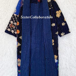 May include: A navy blue patchwork jacket with a collared neckline and open front. The jacket features floral and geometric patterns. The text "Sister Collaboration" is visible on the jacket.