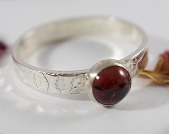 May include: A silver ring with a red gemstone set in the center. The band is decorated with a floral pattern.