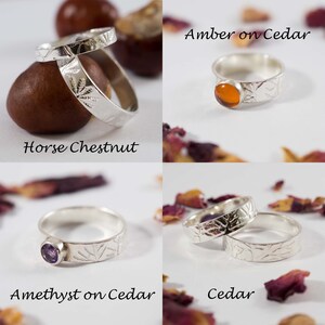 K&ouml;nnte beinhalten: Vier Silberringe mit verschiedenen Steinen und Texturen. Die Ringe werden auf einem wei&szlig;en Hintergrund mit nat&uuml;rlichen Elementen wie Rosskastanien und Rosenbl&uuml;ten pr&auml;sentiert. Die Ringe sind mit "Amber on Cedar", "Amethyst on Cedar", "Cedar" und "Horse Chestnut" beschriftet.