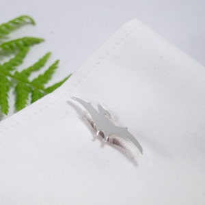 May include: Silver cufflinks shaped like a pterodactyl, a flying dinosaur with a long beak and wings, on a white background.