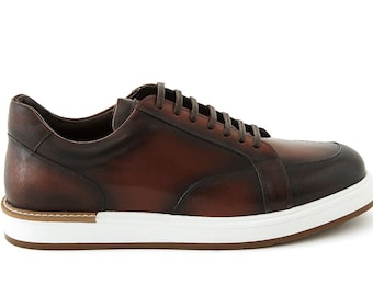 May include: Brown leather sneakers with a white sole and brown laces. The shoes have a classic design with a rounded toe and a low-profile silhouette. The leather has a distressed look.
