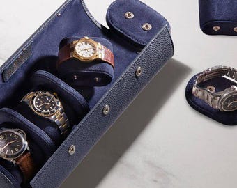 May include: A navy blue leather watch travel case with three watches inside. The case is open, revealing the watches on individual cushions. A separate watch holder and a single watch on a cushion are also visible.