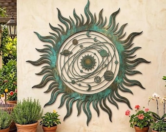 Könnte beinhalten: Ein großes Wandkunstwerk aus Metall in Form eines Sonnenstrahls mit einem Himmelsdesign. Das Kunstwerk zeigt eine zentrale Sonne, Planeten und Sterne in einem kreisförmigen Rahmen mit einer verwitterten Türkis- und Bronzefinish. Der Sonnenstrahl ist an einer cremefarbenen Wand angebracht, umgeben von Topfpflanzen.