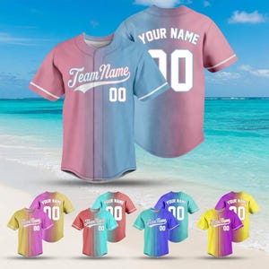 May include: Baseball jerseys in various color combinations, including pink and blue, with the text "Team Name" and "Your Name" and the number "00" or "70". The jerseys have white accents and are displayed on a beach background.