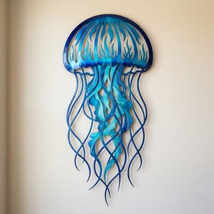 Puede incluir: Una pieza de arte mural de metal azul con forma de medusa. La medusa tiene una parte superior redondeada con diseños recortados y largos tentáculos fluidos. La combinación de colores incluye tonos de azul, creando una estética acuática vibrante. Este artículo decorativo está diseñado para montaje en pared.
