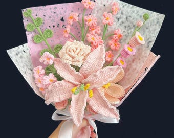 May include: A handcrafted crochet bouquet with pink and peach flowers, including lilies and roses, wrapped in pink and white paper. The bouquet is tied with a white ribbon and pink fringe.